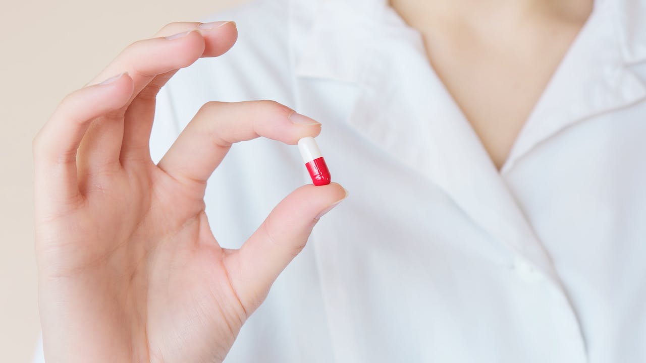 A person holding a red and white antibiotic pill